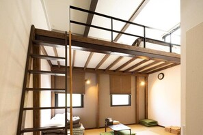 Une pièce de style « loft », avec un plafond orné de poutres en bois, une échelle, un lit, une petite table et une fenêtre.