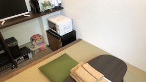 A neatly arranged room with a bed, a small table with a microwave, a television on a shelf, and a trash bin. - Hotel Tohko Hakata Gion (Fukuoka)