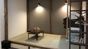 A room with a low wooden ceiling, a small table with folded towels, and a rack with hanging items. - Hotel Tohko Hakata Gion (Fukuoka)