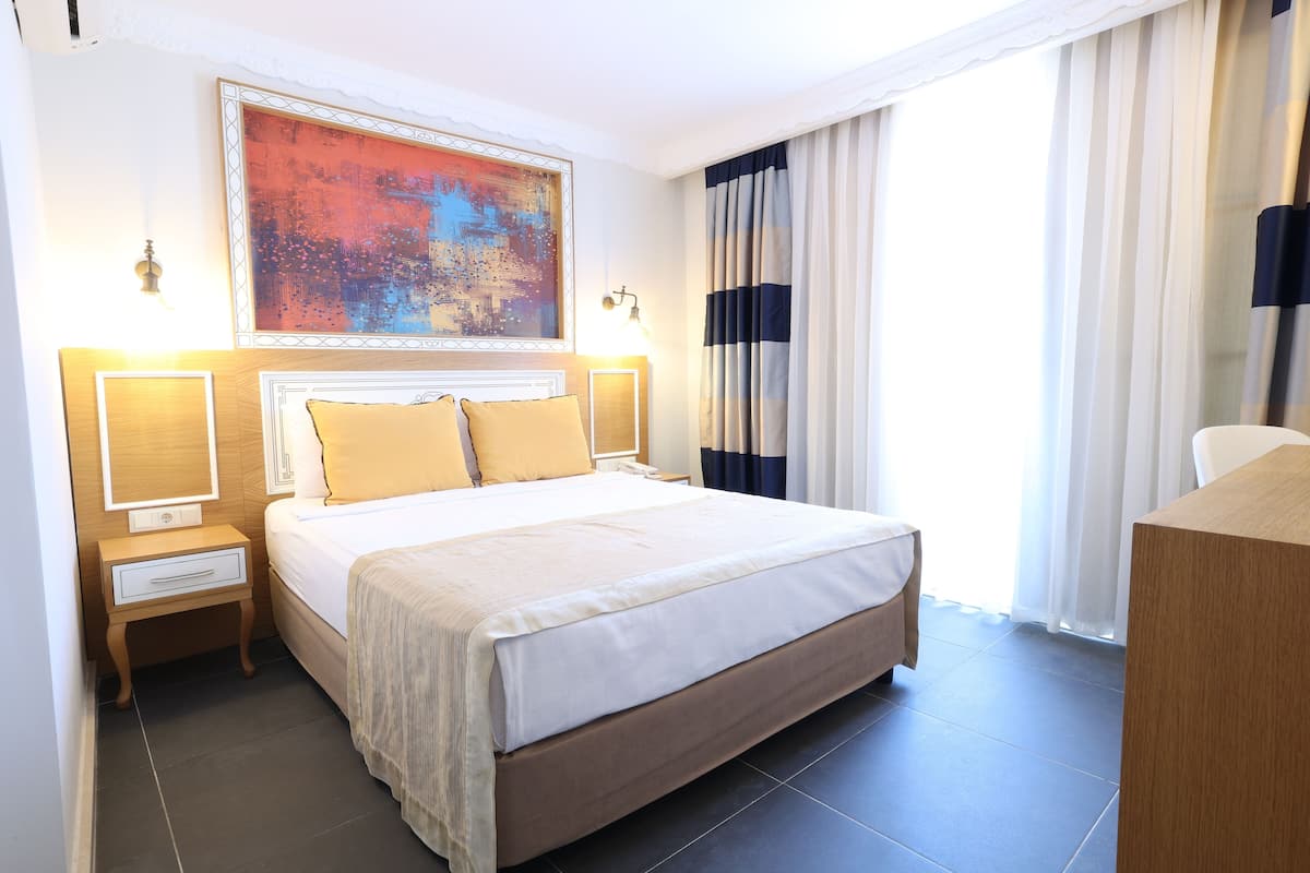Une chambre d’hôtel avec un grand lit, des lampes de chevet, une table de nuit, un tableau au mur et une fenêtre avec des rideaux.