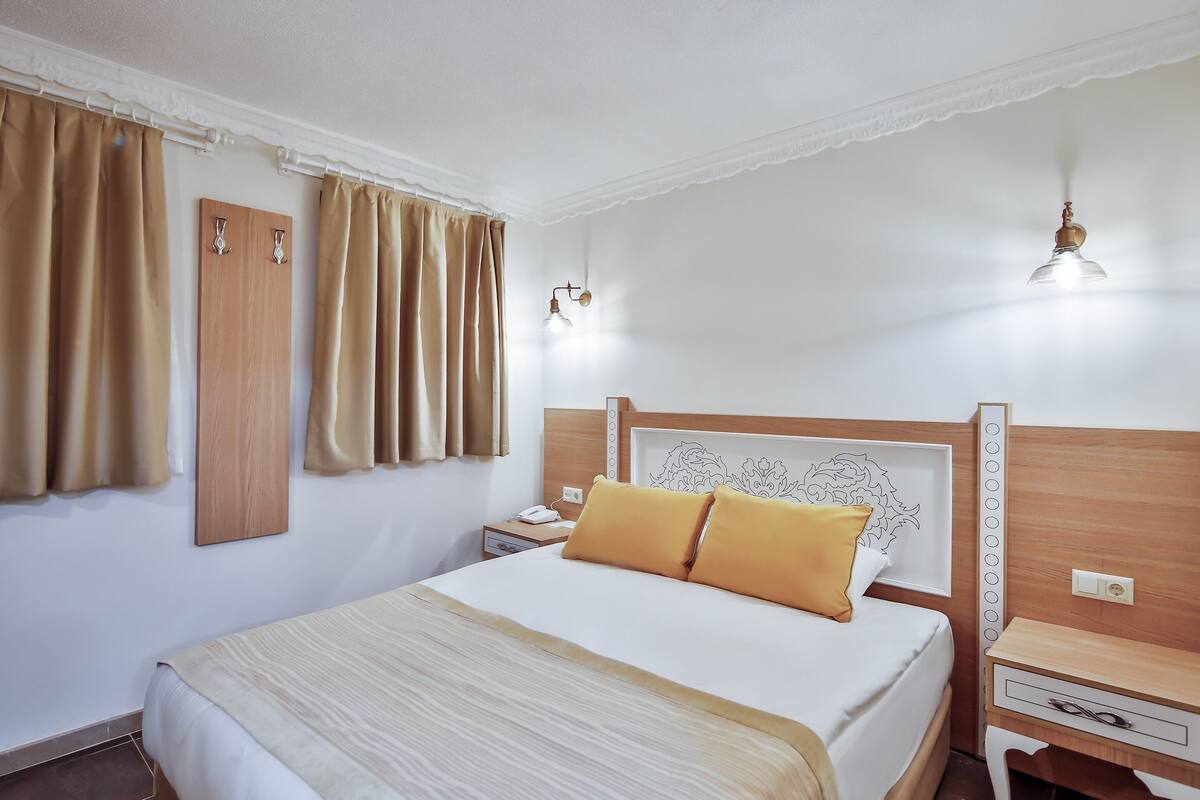 Une chambre d’hôtel bien rangée, avec un lit, des tables de chevet, une petite table et une lampe fixée au mur.