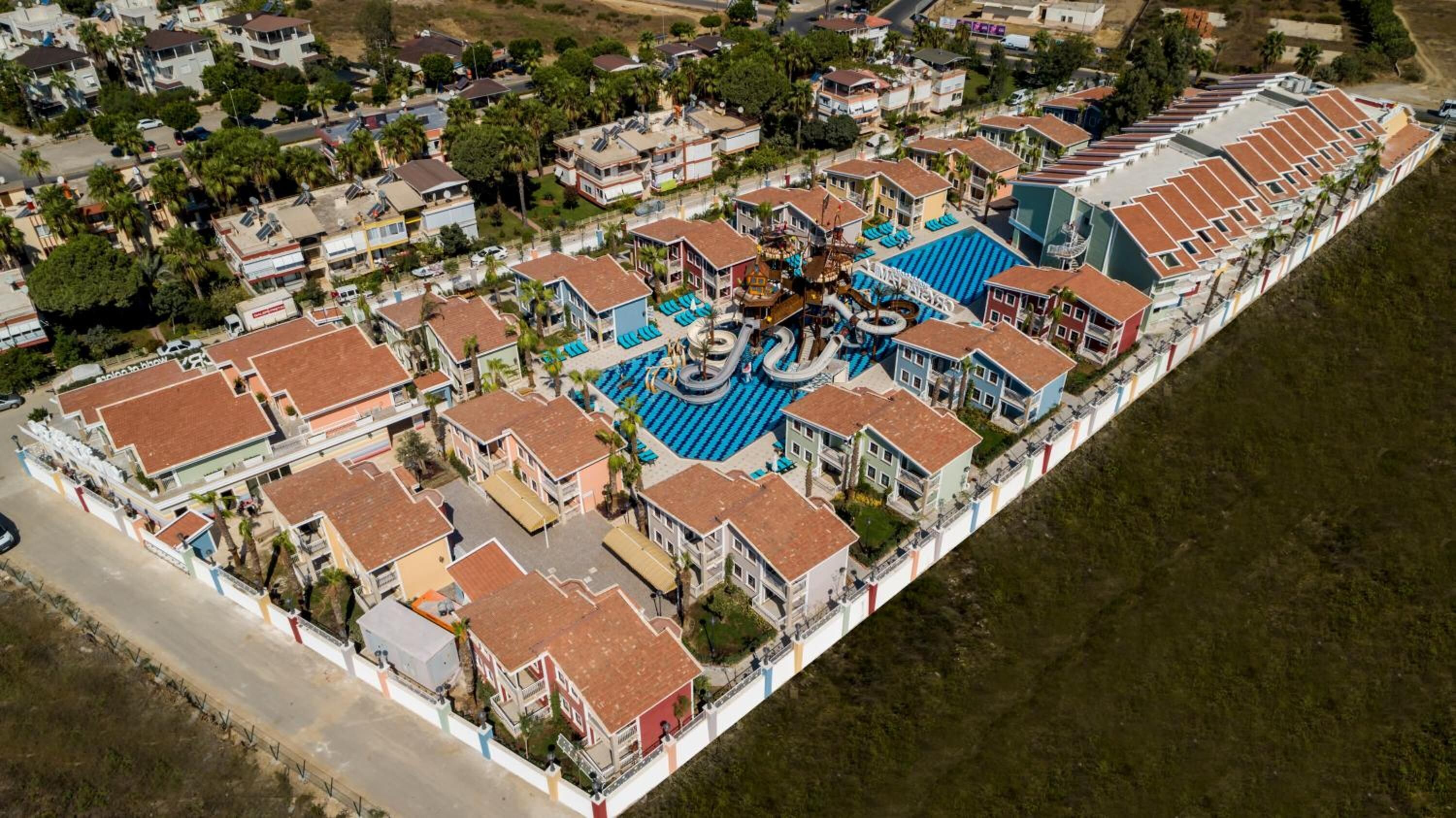 Vista aérea de una zona residencial costera con un amplio complejo de piscinas rodeado de casas de una sola planta con techos de tejas rojas.