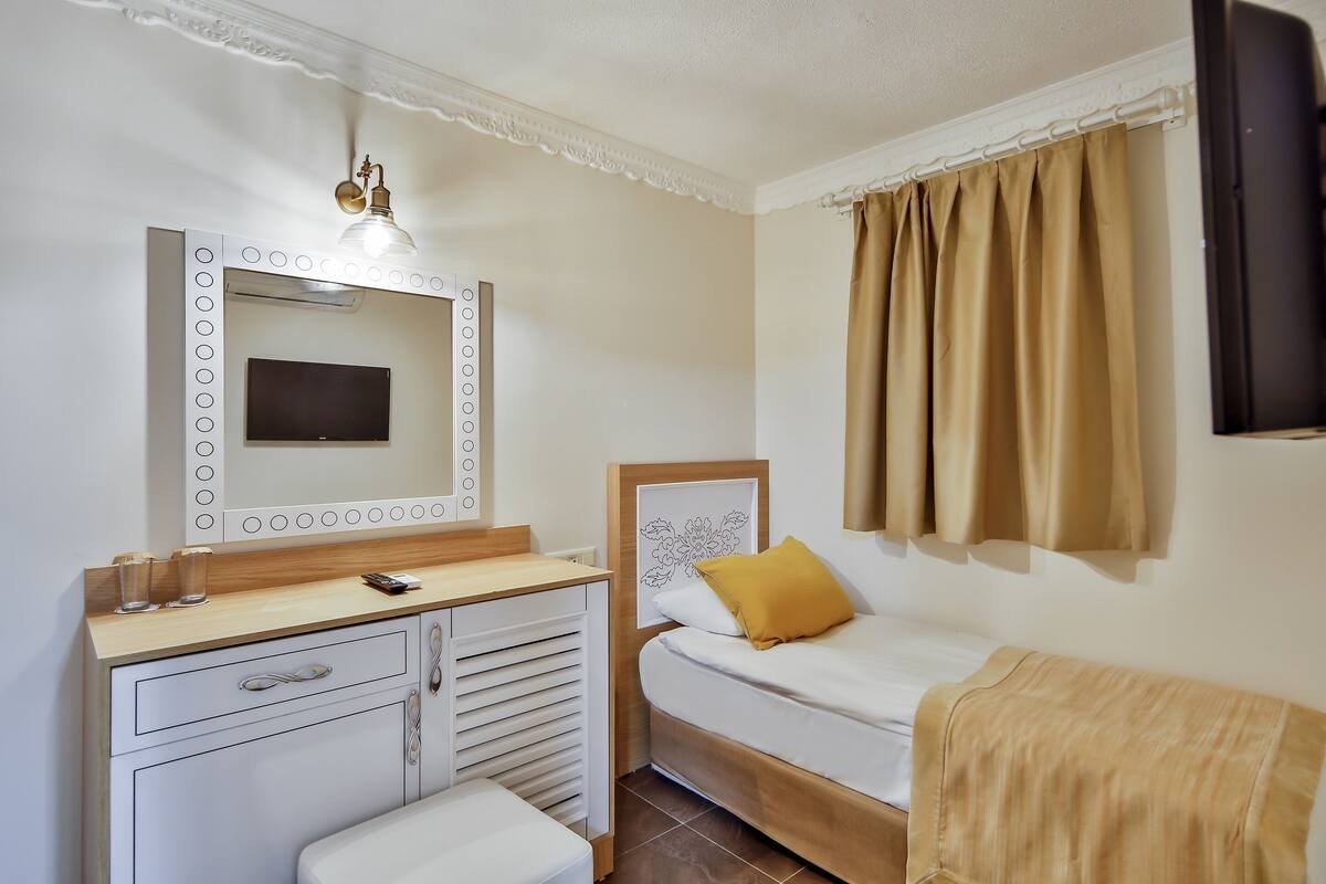 Une chambre à coucher avec un lit, une coiffeuse avec un miroir, une télévision et une fenêtre avec des rideaux.