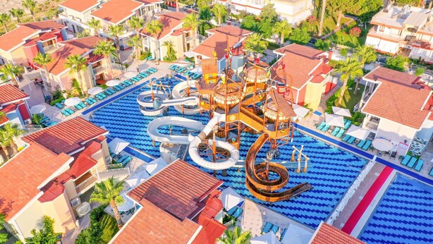 Vista aérea de un complejo turístico con una piscina grande, toboganes de agua y varias edificaciones con tejados de tejas rojas.