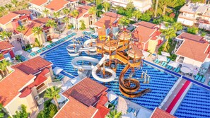 Vue aérienne d’un complexe hôtelier doté d’une grande piscine, de toboggans aquatiques et de plusieurs bâtiments aux toits recouverts de tuiles rouges.