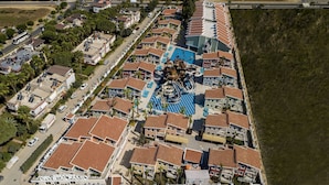 Vista aérea de una zona residencial con varias casas de dos pisos, una piscina central con toboganes y una carretera aledaña.