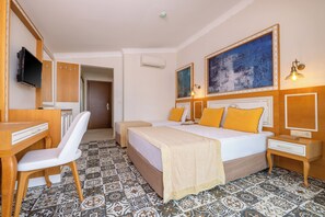 Une chambre d’hôtel comprenant un lit, des tables de chevet, une télévision, un bureau, une chaise et des carreaux de sol à motifs.