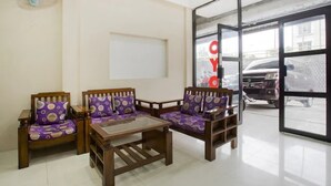 A room with two wooden sofas with purple cushions, a small wooden table, and a large window with a view of parked cars outside. - OYO 3462 Cimindi Residence (Cimahi)