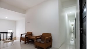A hallway with two wicker chairs and a small table, a staircase with a black railing, and a door leading to another room. - Super OYO Capital O 3463 Cimahi Guest House (Cimahi)