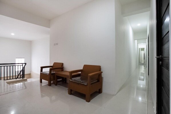 Un pasillo con dos sillones de mimbre y una mesita, una escalera con barandilla negra, y una puerta que da a otra habitación.