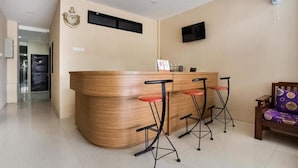 A reception area with a curved wooden counter, three bar stools, a television mounted on the wall, and a fan. - Super OYO Capital O 3463 Cimahi Guest House (Cimahi)