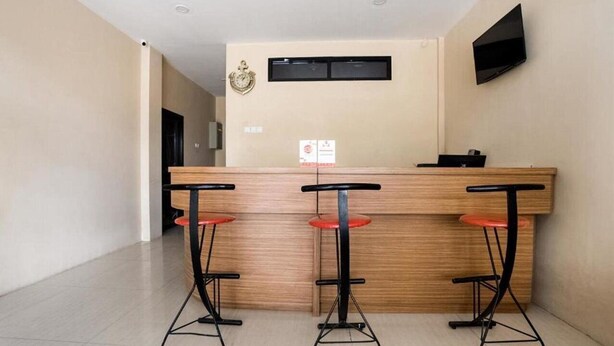 A reception area with a wooden counter, three black bar stools with red seats, a mounted television, and a wall-mounted air conditioning unit. - Super OYO Capital O 3463 Cimahi Guest House (Cimahi)