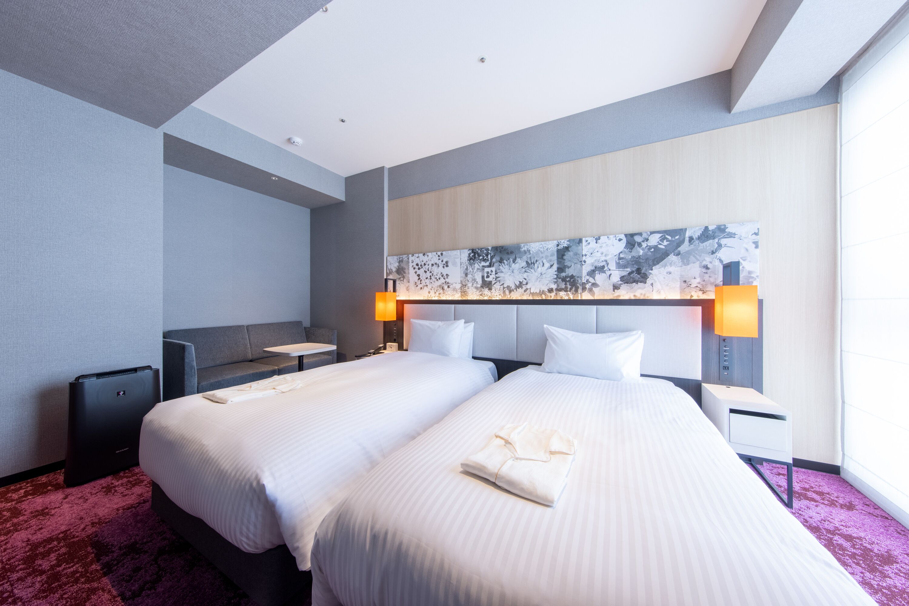 A hotel room with two beds, a large abstract painting on the wall, and a red carpet.