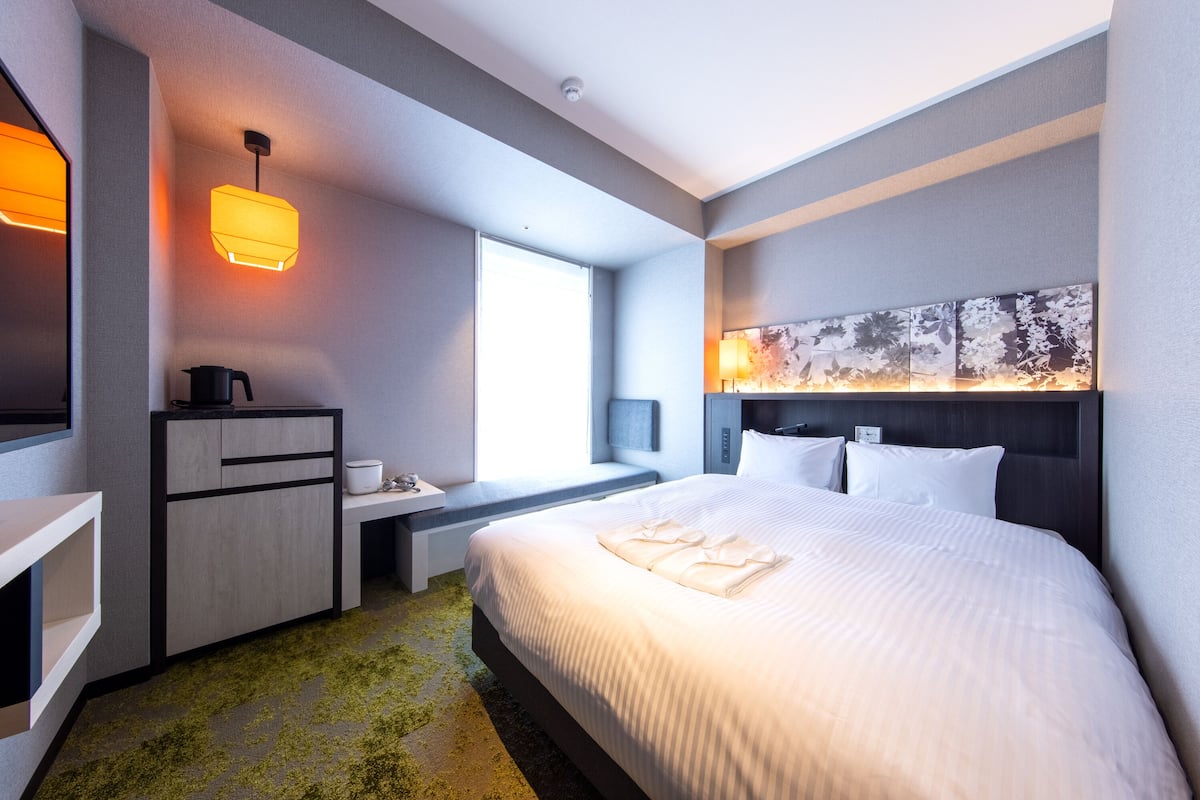 Een moderne hotelkamer met een groot bed, een bureau met stoel, een klein zitgedeelte en een groot raam.