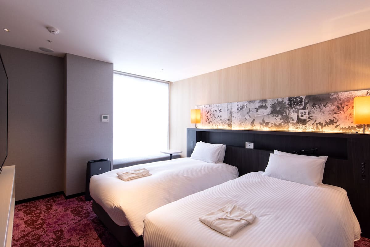 Een hotelkamer met twee bedden, een groot raam, een modern hoofdeinde en een tafeltje.