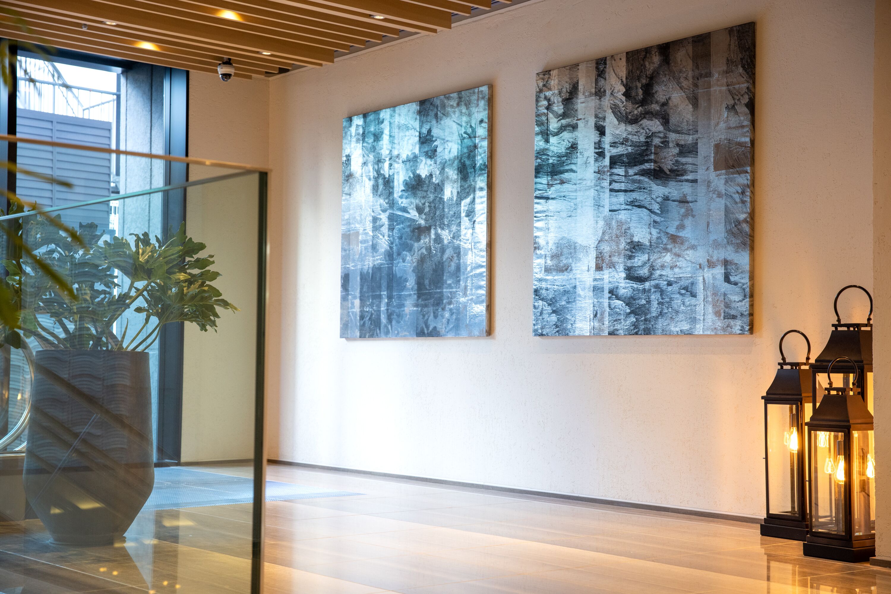 A modern interior with two large abstract paintings, a potted plant, and two lit lanterns.