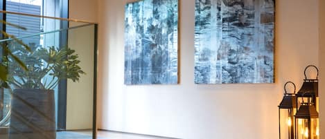 A modern interior with two large abstract paintings, a potted plant, and two lit lanterns.