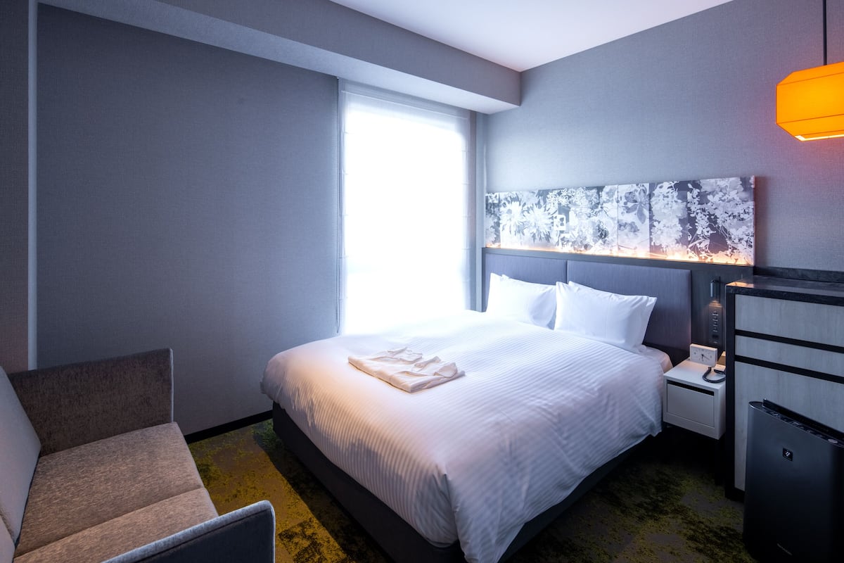 Een hotelkamer met een bed, nachtkastje, bureau, stoel en raam met jaloezieën.