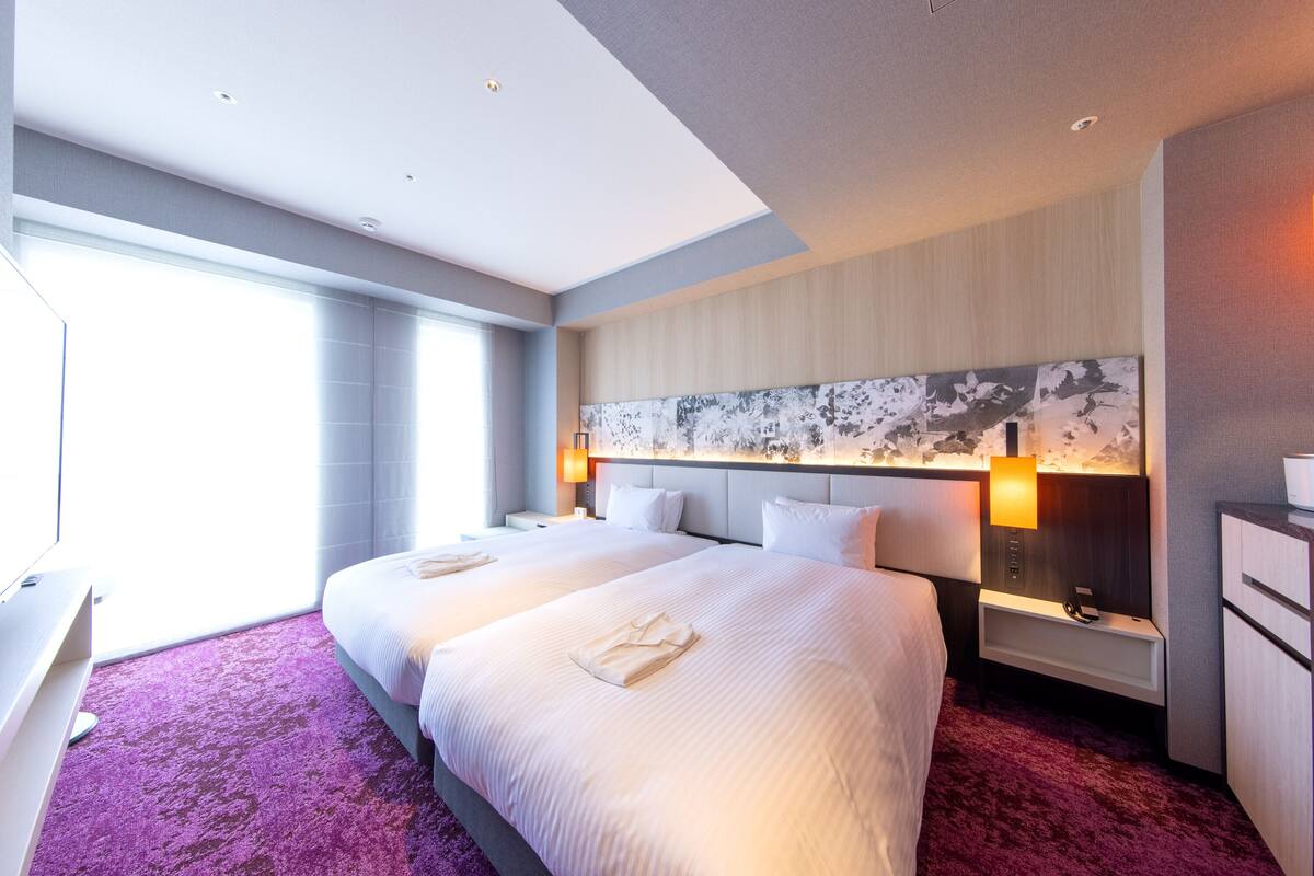 Een hotelkamer met twee bedden, een groot kunstwerk aan de muur en een bureau met een lamp.