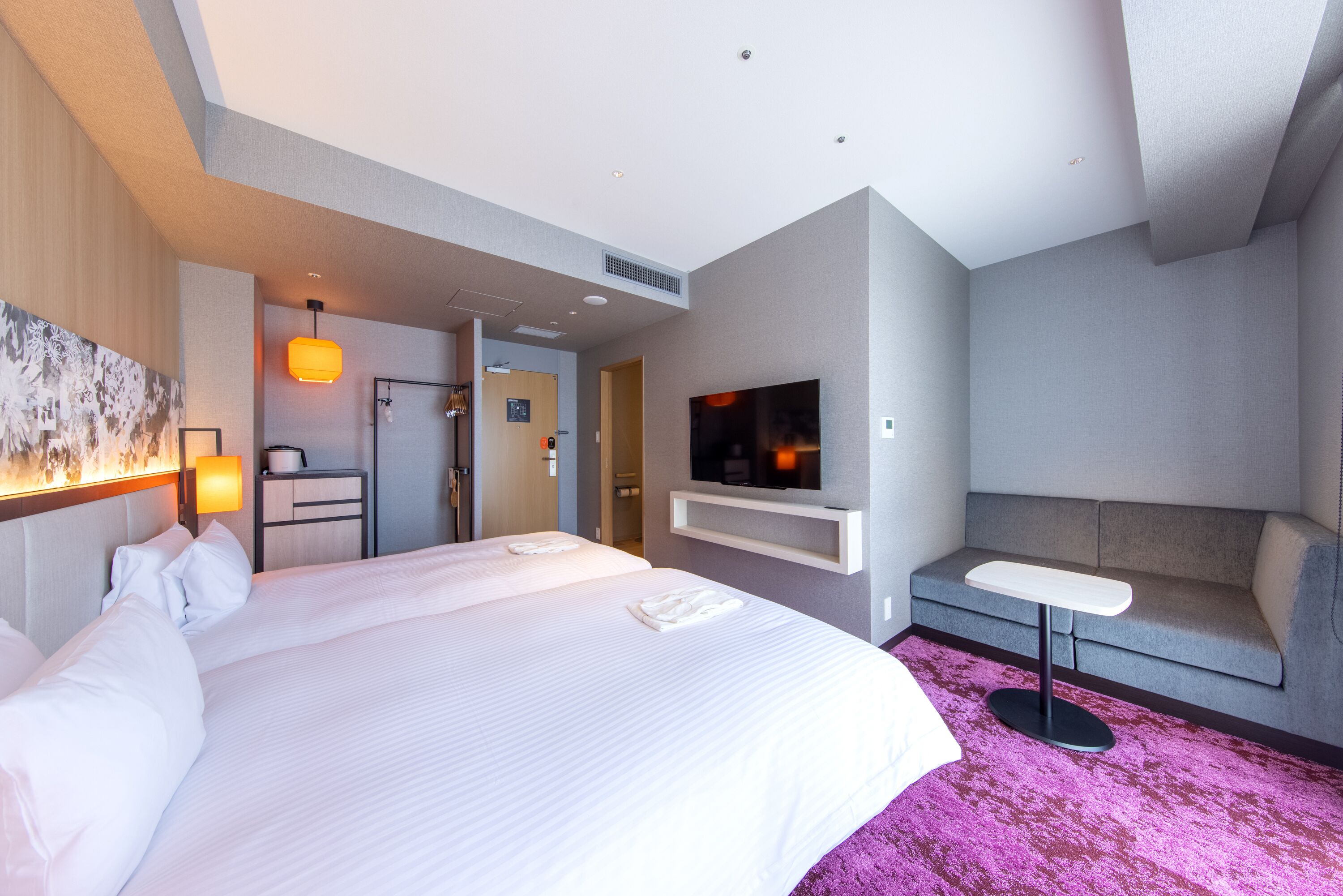 A hotel room with a large bed, a flat-screen TV, a sofa, and a small table.