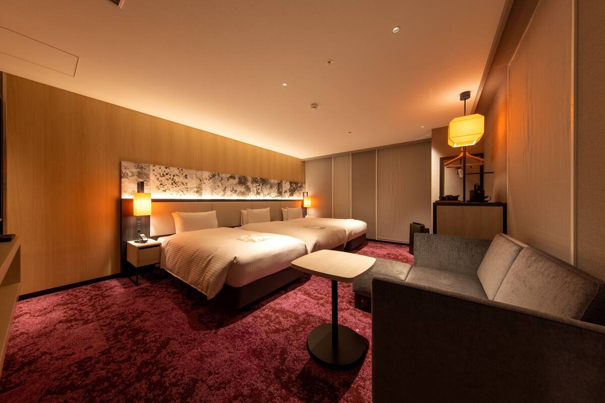 Een hotelkamer met twee bedden, een kleine tafel, een bank en een groot kunstwerk aan de muur.