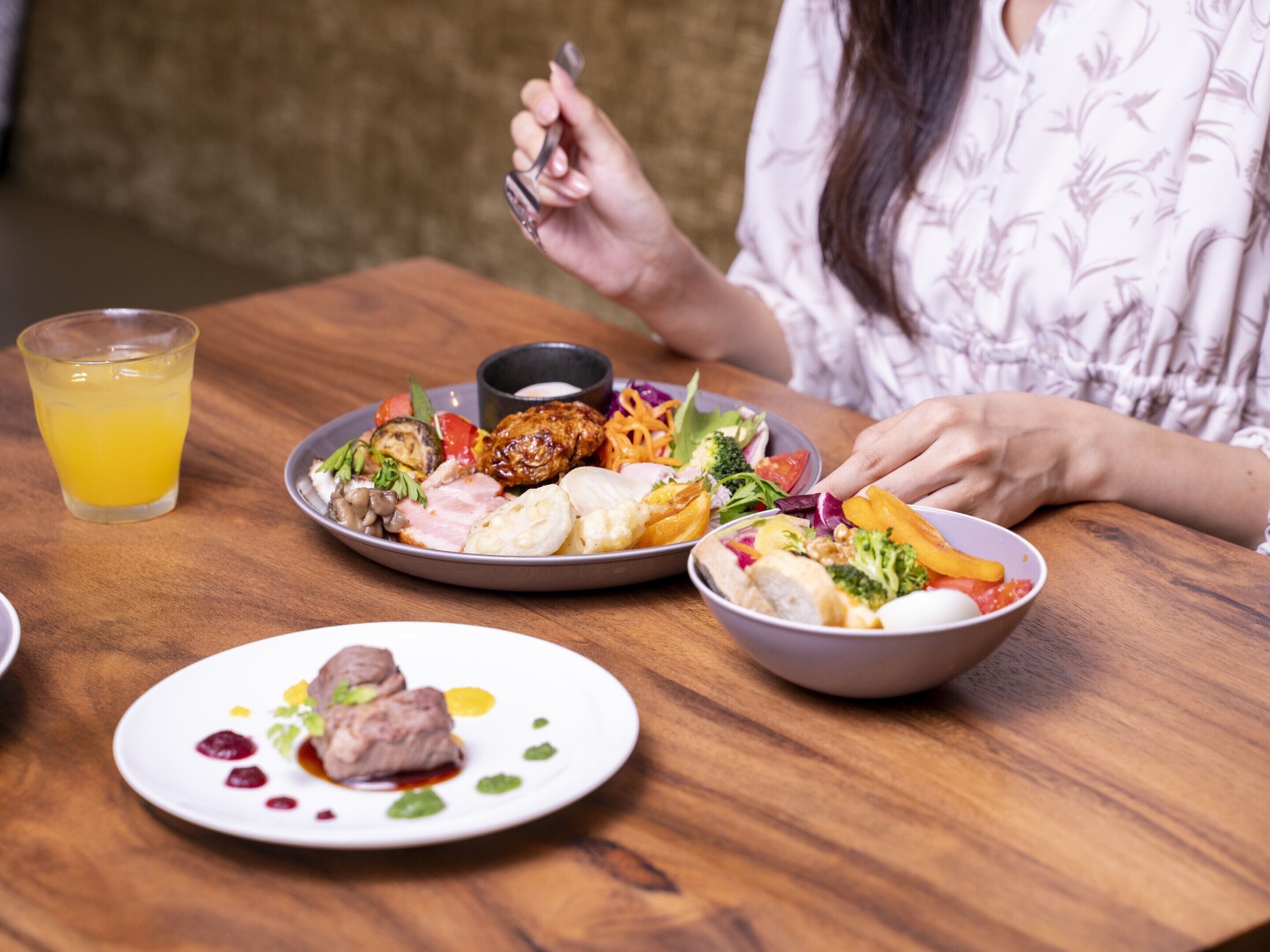 A dining table with various dishes, a glass of orange juice, and a person sitting at the table.