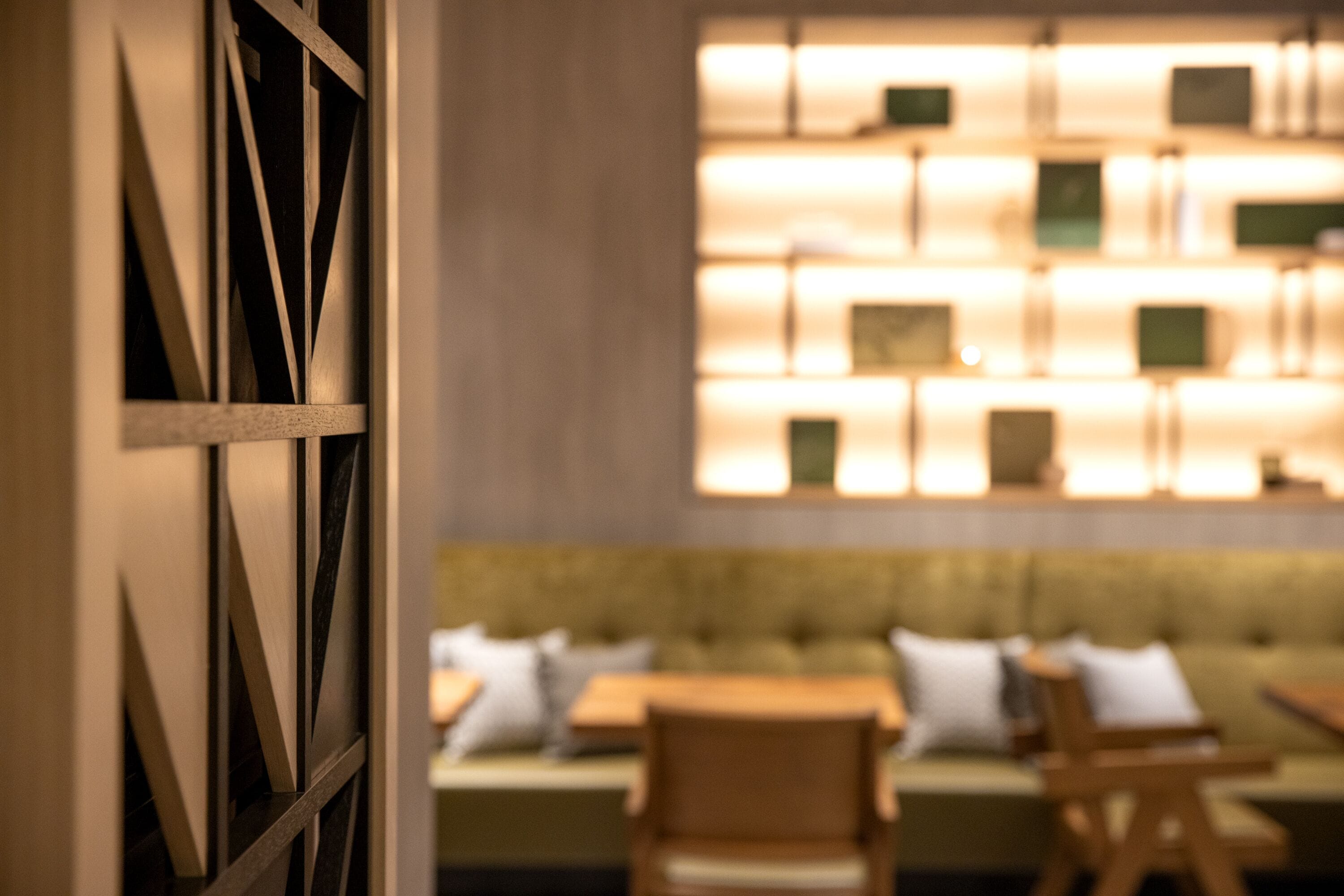 A modern interior with a seating area featuring a sofa and chairs, a wooden partition with geometric patterns, and a wall with illuminated panels.