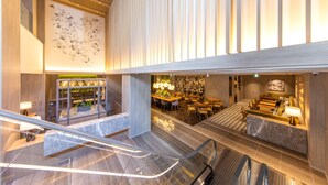 Un hall d’hôtel moderne avec un escalier central, un espace repas et un comptoir d’accueil.