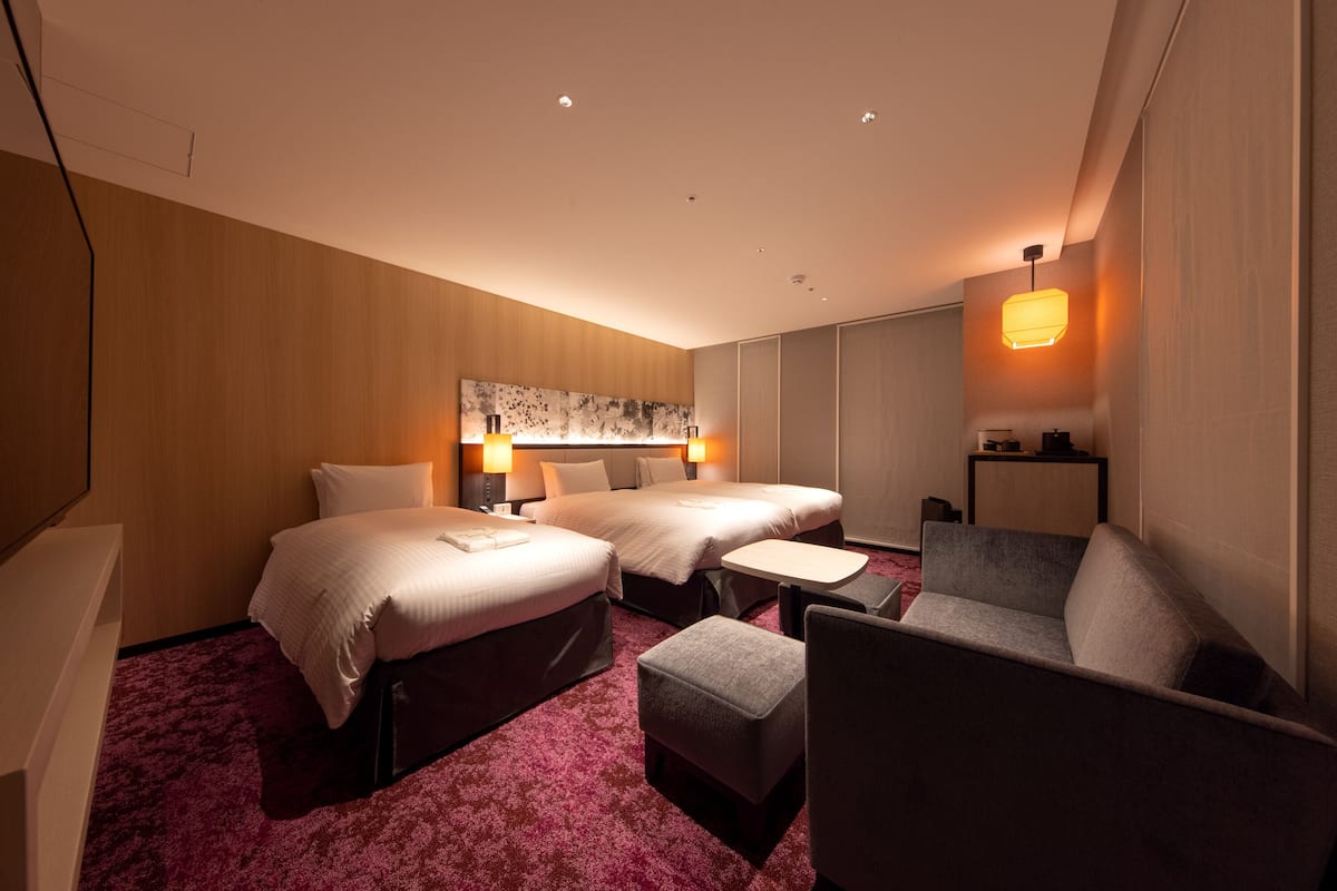 Een hotelkamer met twee bedden, een kleine tafel, een bank en een wandlamp.