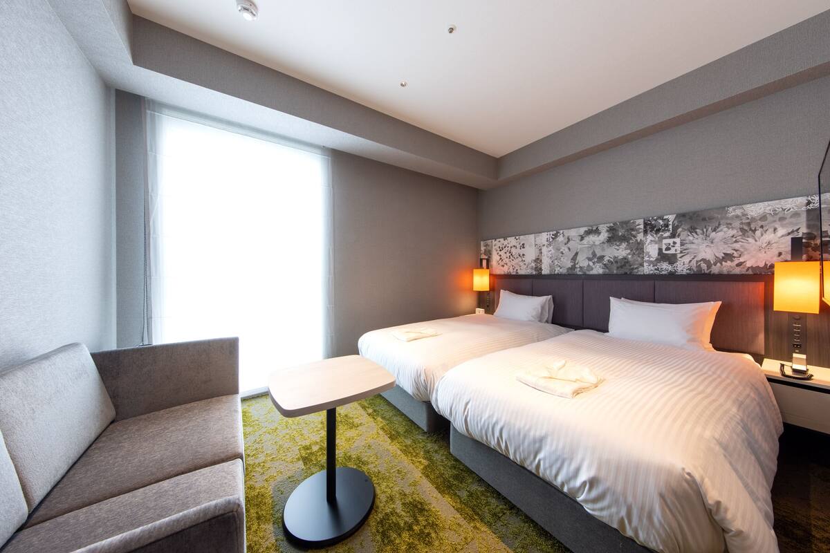 Een hotelkamer met een groot bed, twee nachtkastjes met lampen, een bank en een raam dat natuurlijk licht biedt.