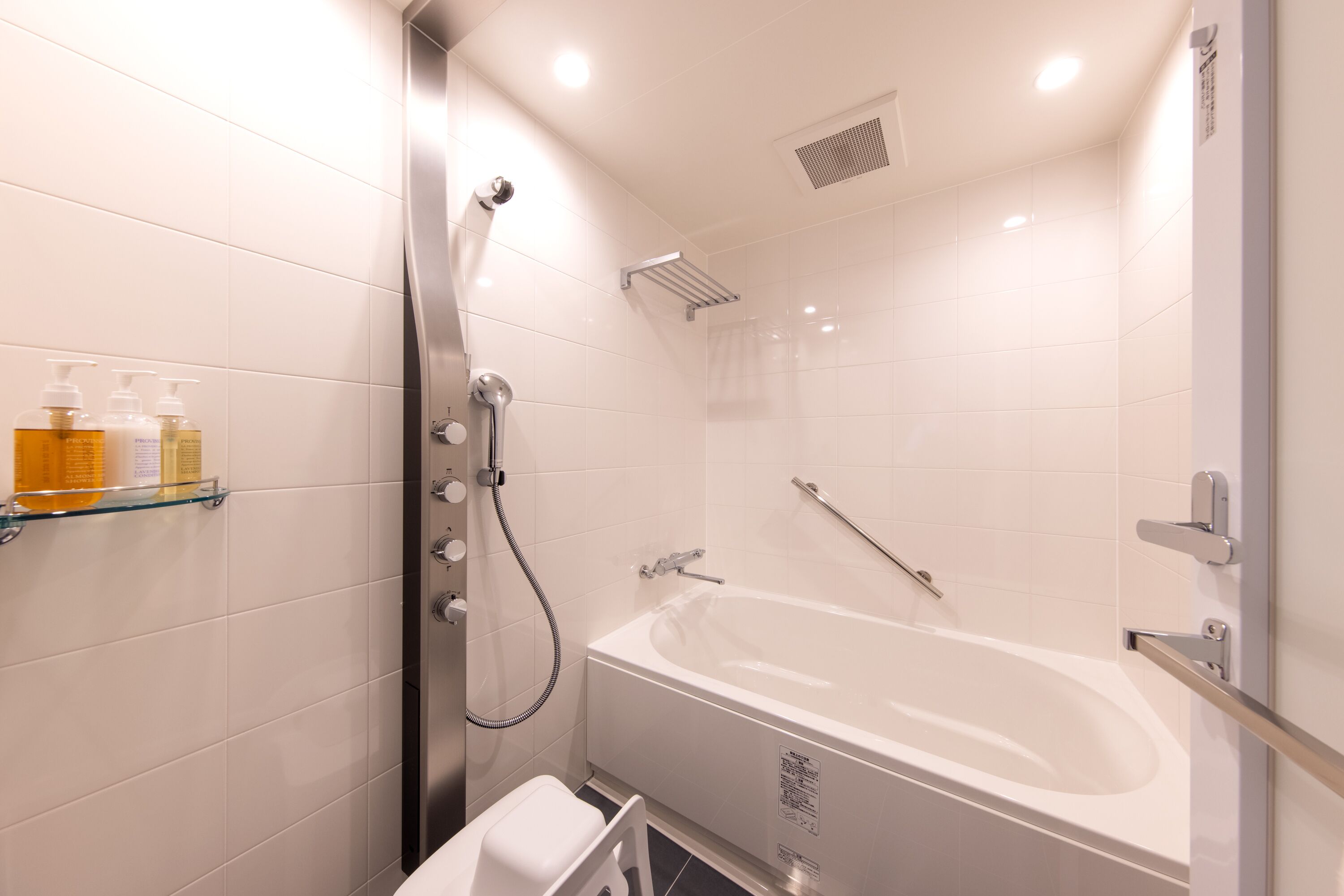 A modern bathroom with a bathtub, shower, and glass shelves with toiletries.