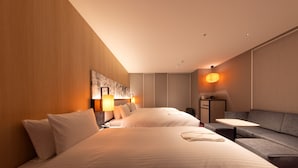 Une chambre d’hôtel avec deux lits, un canapé, une petite table et une œuvre d’art accrochée au mur.