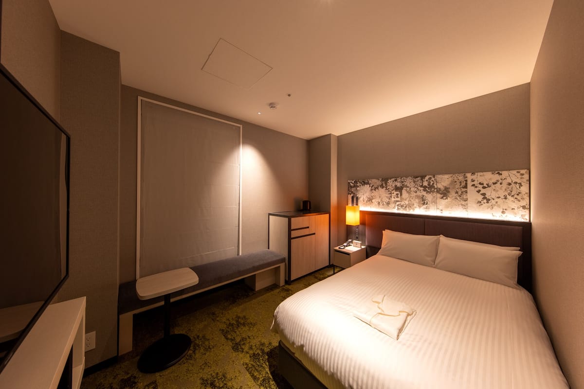 Een hotelkamer met een bed, een bureau, een bankje, een nachtkastje en een wandlamp.
