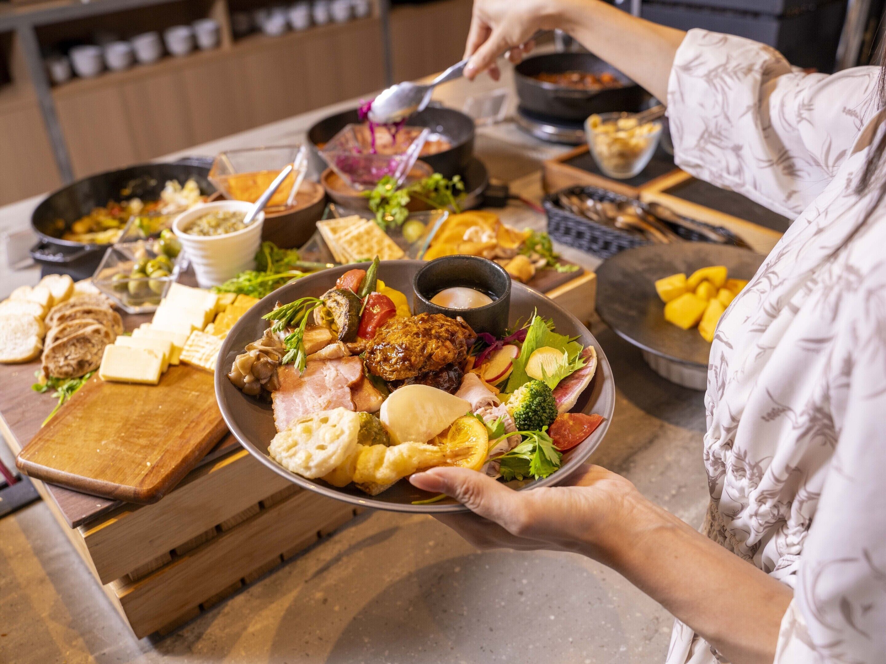 A person holding a plate with various foods, including meats, cheeses, and vegetables, at a buffet table.