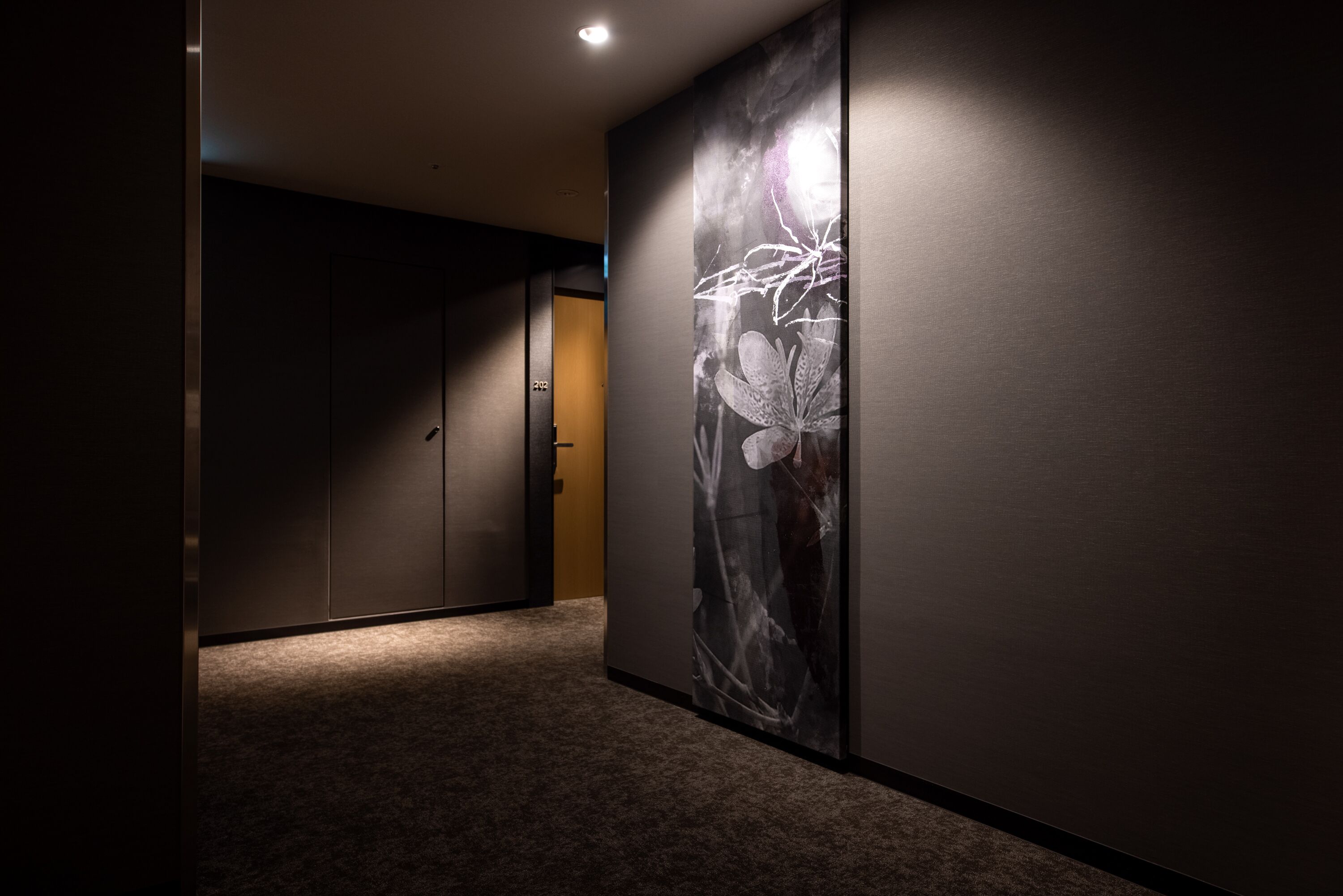 A hallway with a dark wall and a large floral artwork on one side.