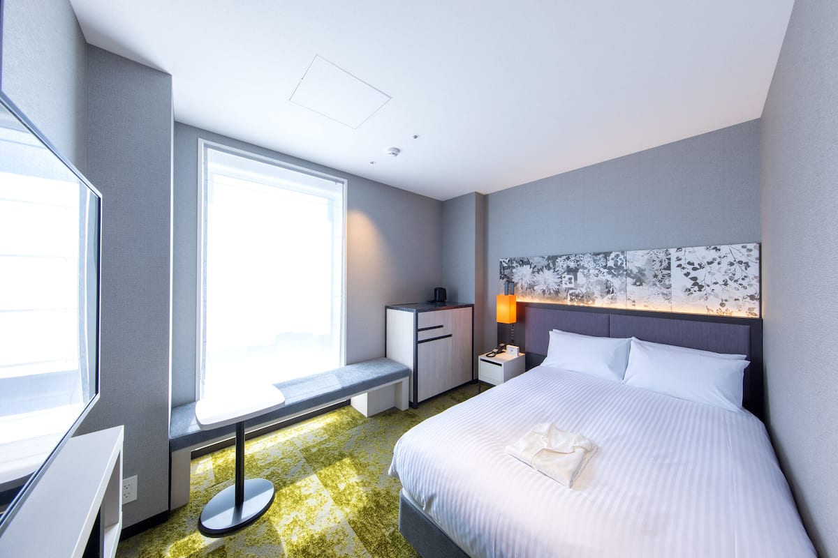 Een hotelkamer met een groot bed, een bureau, een stoel, een bankje en een raam.