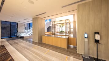 Eine moderne Hotelhalle mit einer Rezeption, einem digitalen Kiosk und Blick ins Freie.