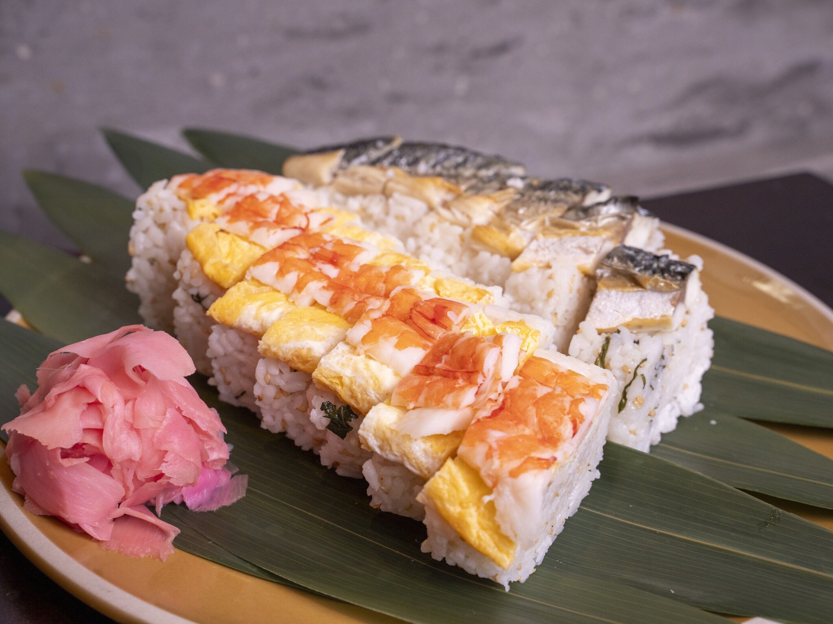A plate of sushi with fish, egg, and rice, accompanied by pickled ginger and wasabi.