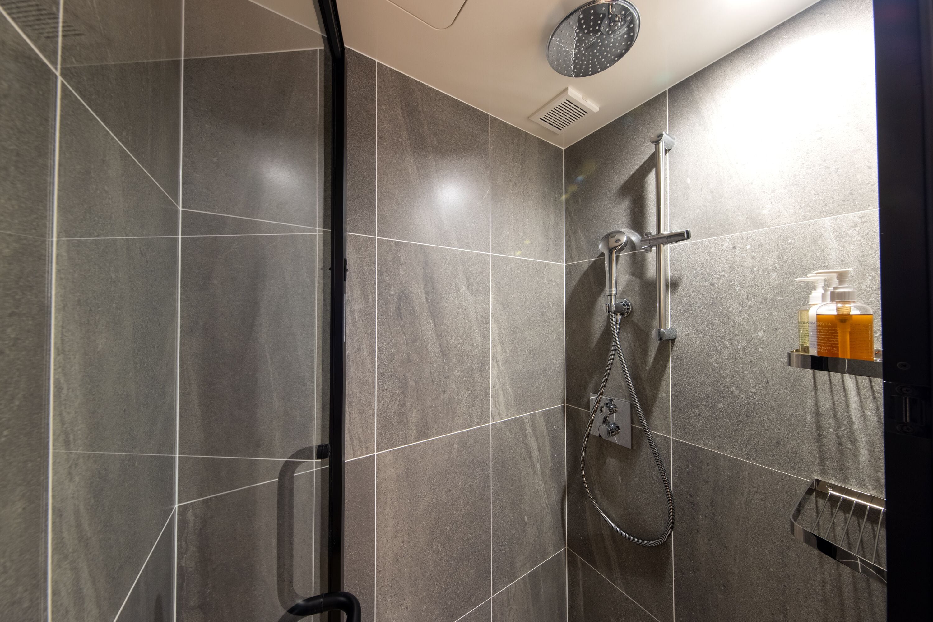 A modern shower area with a handheld showerhead, a wall-mounted faucet, and a glass shower enclosure.