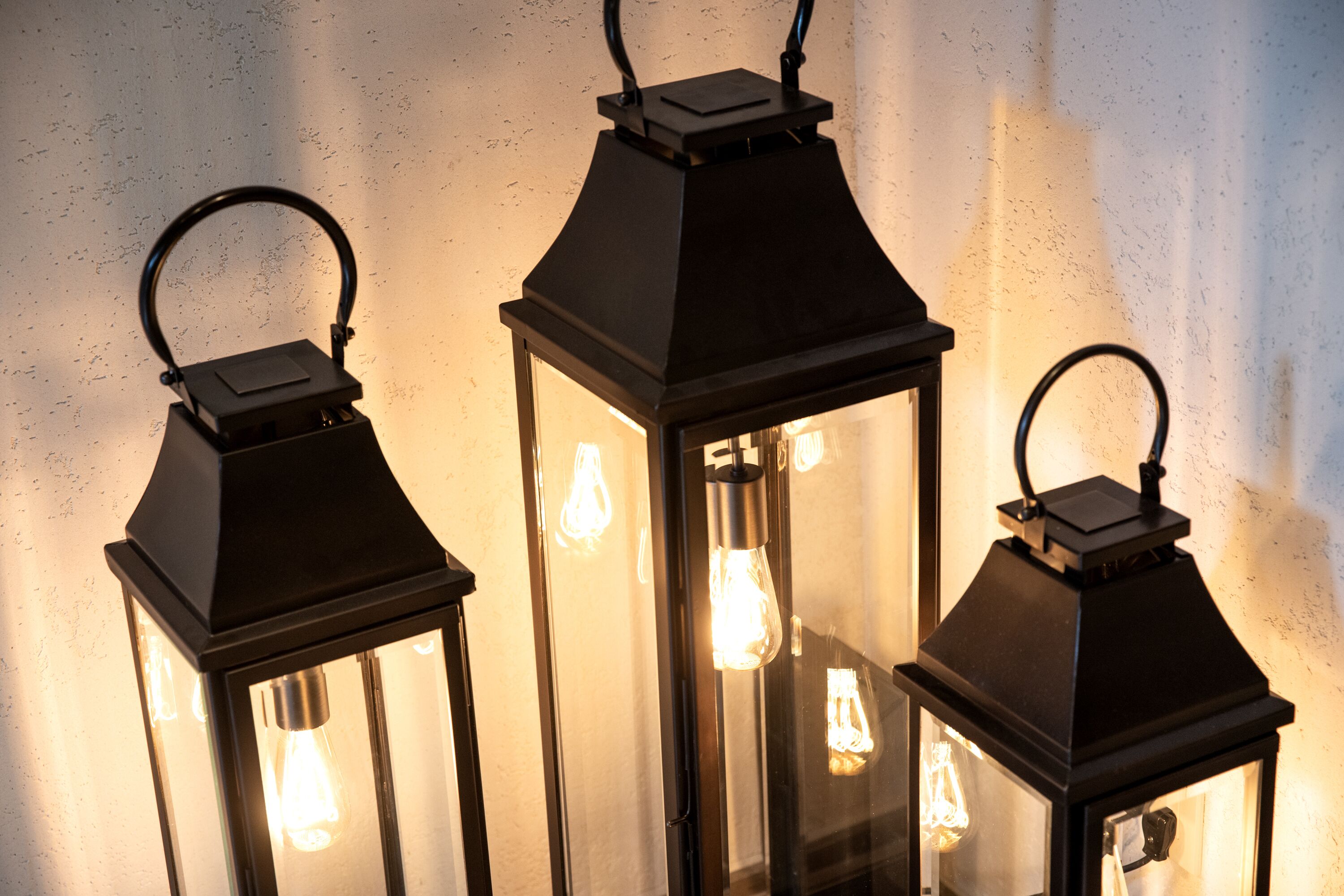 Three black lantern-style lights with exposed filament bulbs against a textured wall.