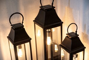 Three black lantern-style lights with exposed filament bulbs against a textured wall.