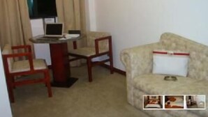 A small room with a beige sofa, a wooden chair, a small table with a laptop, and a window with curtains. - Maxim Plaza Hotel (Juiz de Fora)