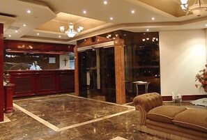 Um hall de entrada com piso de mármore, balcão de recepção, lustre e um sofá.