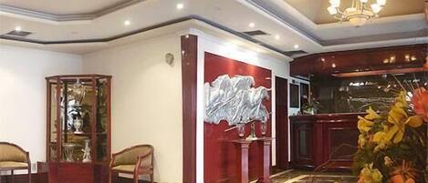 A lobby with a glass display case, a red accent wall, a chandelier, and a floral arrangement.