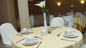 A round table set for a meal with white tablecloths, white chairs, and a vase with a white flower. - Maxim Plaza Hotel (Juiz de Fora)