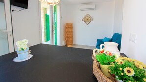 Un salon moderne avec un téléviseur à écran plat fixé au mur, une grande table sombre et une table basse en osier agrémentée de fleurs.