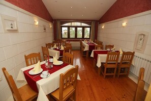 Un espace repas comprenant plusieurs tables et chaises, disposées en ligne, avec vue sur l’extérieur grâce à une grande fenêtre.