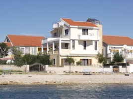 A multi-story building with balconies, a swimming pool, and a beachside location.
