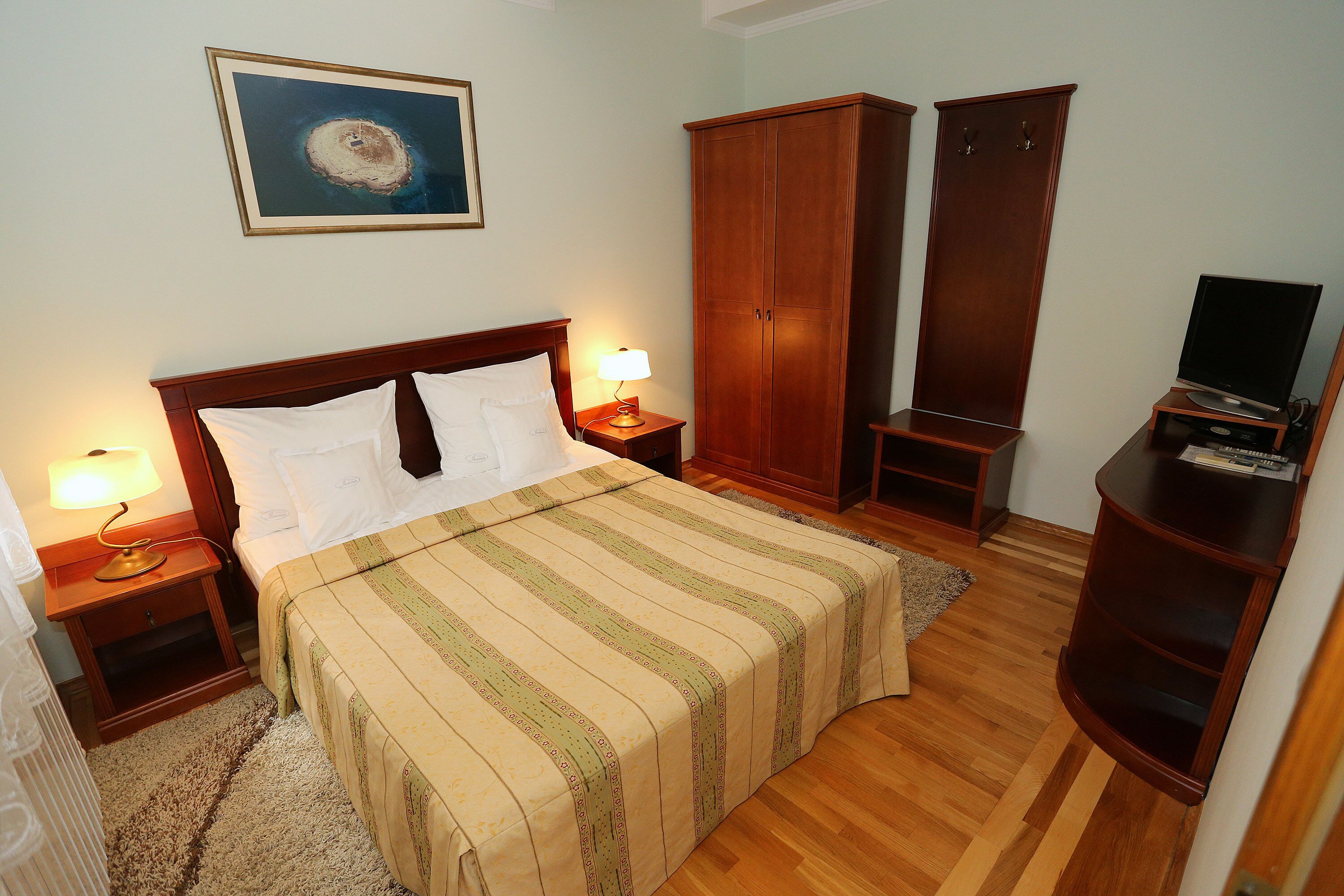 Quarto bem arrumado com cama, luminárias de cabeceira, televisão e guarda-roupa.