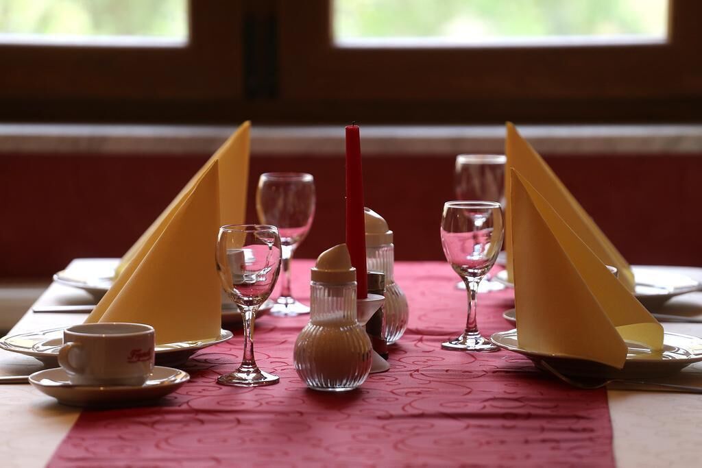 Mesa lista para comer con mantel rosa, copas transparentes y sujetavasos amarillos.
